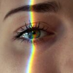 Closeup of crop anonymous sad female with green eyes and rainbow light on face looking at camera