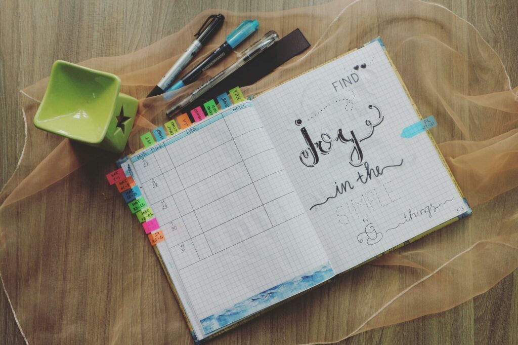 Flat lay of an open bullet journal with pens on a wooden desk, expressing creativity and planning.
